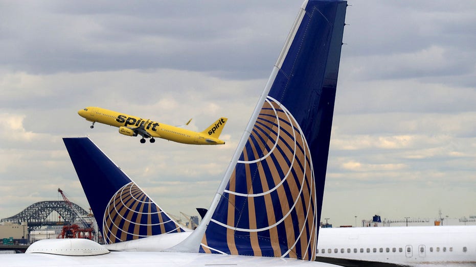 A Spirit Airlines jet takes off above two United Airlines airplanes